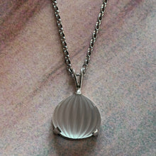 Load image into Gallery viewer, A silver chain necklace with a ribbed, teardrop-shaped translucent pendant, displayed on a textured, mottled pink and gray surface.
